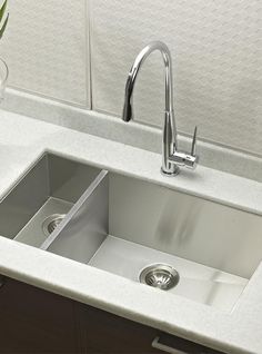 a stainless steel kitchen sink and faucet in a white countertop with a potted plant next to it