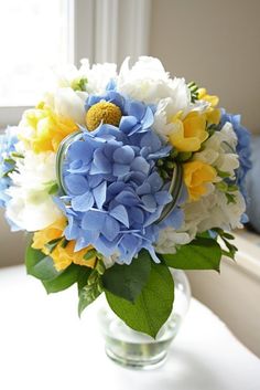 a vase filled with blue, white and yellow flowers on top of a window sill