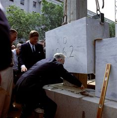 two men in suits and ties are placing something into a cement box on the ground