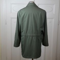 This 1990s European vintage olive green jacket has a wide wing collar that you can also turn up and buckle closed. The jacket has padded shoulders, closes in the front with five concealed buttons, and has a elasticated inner drawstring at the waist. A silicone finish on the outside of the jacket means that it is water-resistant. The jacket is lined in a gold satin polyester fabric. Note that this jacket originally had a hood attached by a zipper (under the collar), but the hood is no longer avai Vintage Green Long Sleeve Parka, Green Workwear Parka With Pockets, Green Parka With Pockets For Work, Vintage Olive Long Sleeve Outerwear, Military Style Long Sleeve Parka For Workwear, Olive Vintage Long Sleeve Outerwear, Green Workwear Parka, Military Style Green Outerwear For Work, Green Military Style Workwear Outerwear