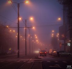 cars are driving down the street on a foggy night in an urban area with traffic lights