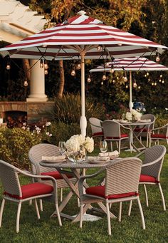 an outdoor dining set with umbrellas and chairs on the grass in front of a gazebo