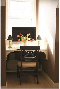 a desk with a computer on top of it next to a lamp and flowers in a vase