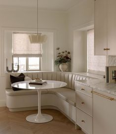 a white kitchen with a round table in the center and an oval bench at the end