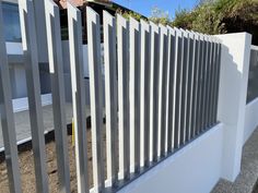 a white fence with vertical slats on the top and bottom, in front of a house