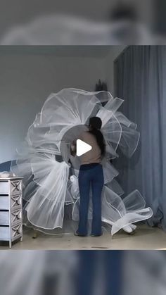 a woman is standing in front of a bed with white netting on it and she has her arms wrapped around the head