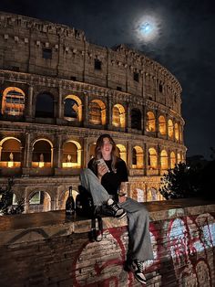 a woman sitting on top of a brick wall next to an old building at night