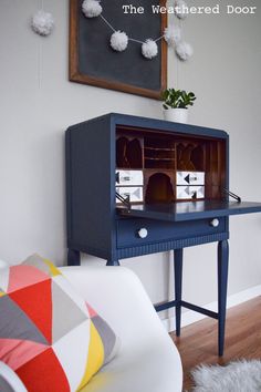 a blue desk with a toy house in the top drawer and some pom poms hanging from it