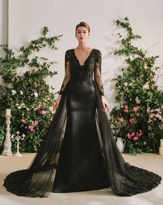 a woman in a long black dress standing next to flowers