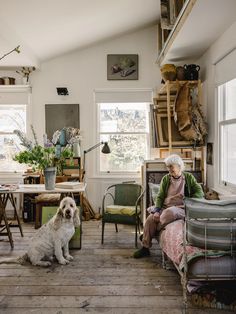 an older woman sitting on a couch next to a dog in a room filled with furniture