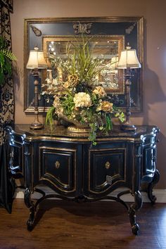 an ornate black and gold sideboard with flowers on it in front of a mirror