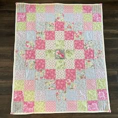 a pink and green patchwork quilt on a wooden floor