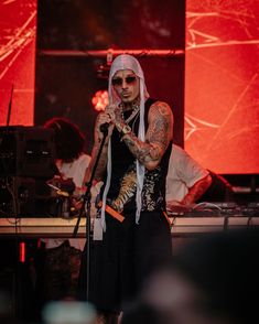 a man with tattoos on his arm and head standing in front of a microphone at a concert