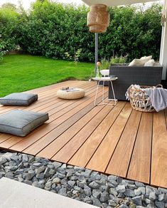 a wooden deck with cushions and pillows on it in front of a green grass area