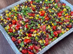 a tray filled with black beans, corn and cilantro salad on top of a wooden table