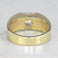 a yellow gold wedding band with a diamond in the center on a white marble surface