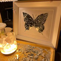 a glass with ice in it sitting on a table next to a framed butterfly artwork