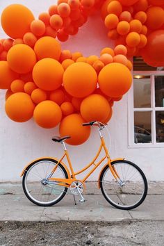 an orange bike parked in front of a building with balloons attached to the side of it