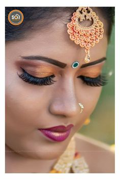 a woman with makeup and jewelry on her face, looking down at the viewer's eye