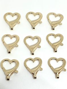 six gold heart shaped hooks on a white surface