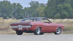 an old red muscle car parked on the side of the road