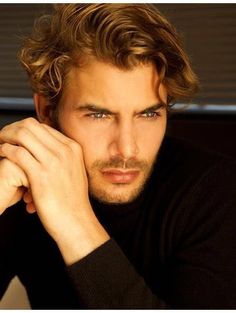 a close up of a person wearing a black shirt and holding his hand on his chin