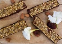 three pieces of granola on a wooden cutting board with nuts and flowers around them