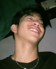 a young man is smiling and wearing a black t - shirt with silver chains around his neck