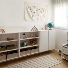 a living room with a white bookcase and various items on the shelves in front of a window