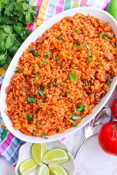 mexican rice in a white dish with tomatoes, cilantro and limes on the side