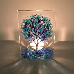 a glass block with a blue tree in the center on a white surface, lit by a candle