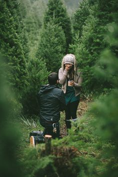 two people standing in the middle of a pine tree forest looking at something on their cell phone