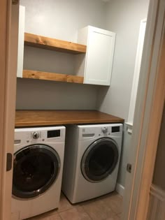 a washer and dryer in a small room with open shelves on the wall