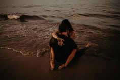 a man and woman sitting on the beach hugging in front of the ocean at night