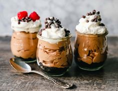 three desserts with whipped cream, chocolate and cherries in glass jars on a wooden table