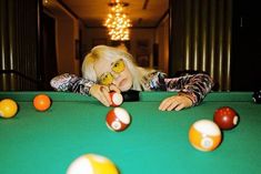 a woman leaning over a pool table with balls in front of her and looking at the camera