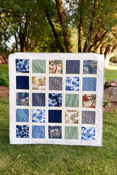 a blue and green patchwork quilt sitting on top of a grass covered field with trees in the background