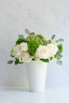 a white vase filled with green and white flowers