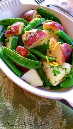 a white bowl filled with green beans and potatoes on top of a tablecloth next to a fork