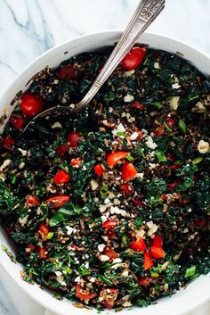 a white bowl filled with spinach, tomatoes and feta cheese next to a spoon