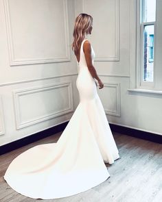 a woman in a white wedding dress standing by a window with her back turned to the camera