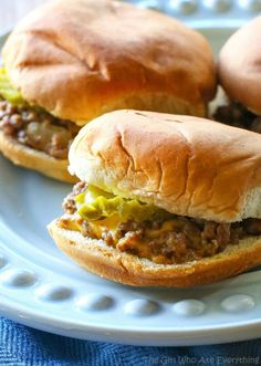 two sloppy joe sandwiches on a plate with a blue towel in the backgroud