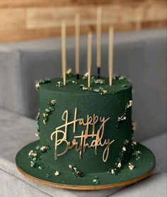 a green birthday cake with gold letters and sprinkles sitting on a table