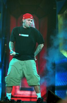 a man standing on top of a stage with his hands in his pockets and wearing a red hat