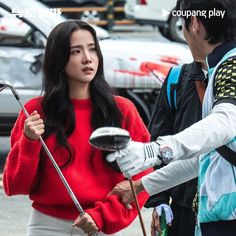 a woman holding an umbrella while standing next to a man in a red sweater and white pants