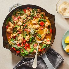 a skillet filled with chicken and vegetables next to lemons on a white table