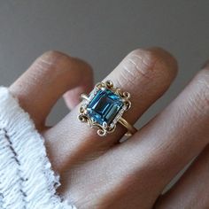 Read about our payment plans before proceeding. Make a lasting impression with the Isis London Blue Topaz Scroll Diamond Ring and its saturated deep blue color. Crafted from 14K gold or 18K solid gold, this stunning piece features a natural london blue topaz centerpiece and delicate baguette diamonds, inspired by the iconic architecture of New York City. All order comes in a Tippy Taste ring box. This ring is handmade and designed in NYC. 14K or 18K solid gold Natural 9*7mm London Blue Topaz Nat Blue Sapphire Topaz Ring With Diamond Cut, Gold Solitaire Blue Topaz Ring, Yellow Gold Diamond Cut Blue Topaz Ring, Blue Topaz Ring With Emerald Diamond Cut, Blue Topaz 14k Gold Promise Ring, Emerald-cut Blue Topaz Ring With Diamond Cut, Blue Emerald-cut Topaz Ring With Diamond Cut, Blue Topaz Ring With Emerald Cut And Diamond Detail, Heirloom Gold Topaz Ring With Blue Topaz