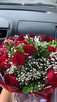 a bouquet of red roses sitting in the passenger seat of a car with baby's breath