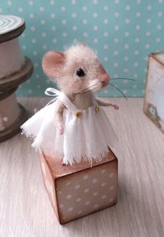 a toy mouse in a white dress sitting on top of a wooden block