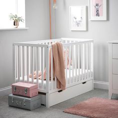 a white crib with pink and grey accessories in a nursery room, next to a window